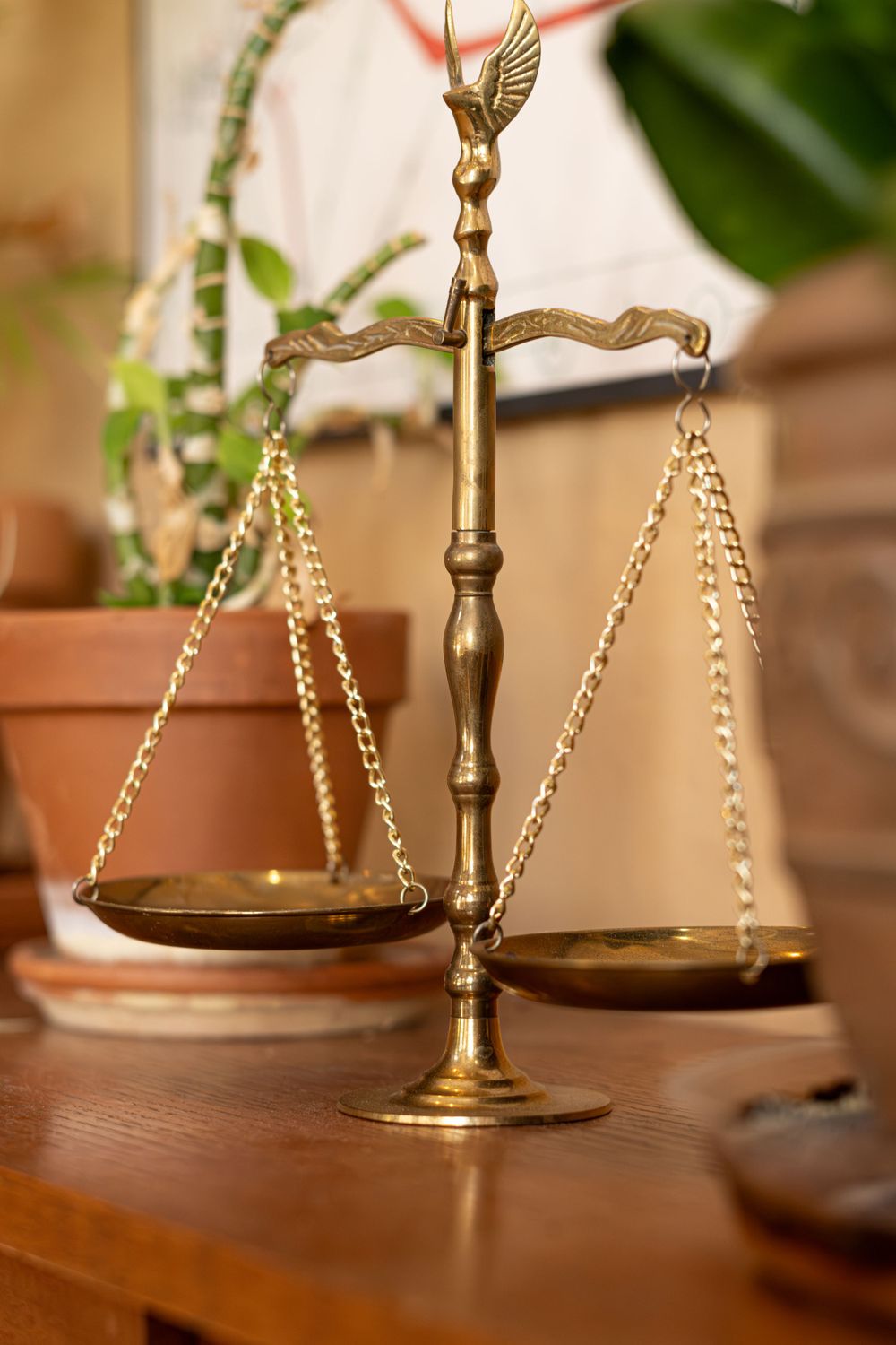 Decorative brass scales of justice with ornate eagle top stand on wooden table near plants.