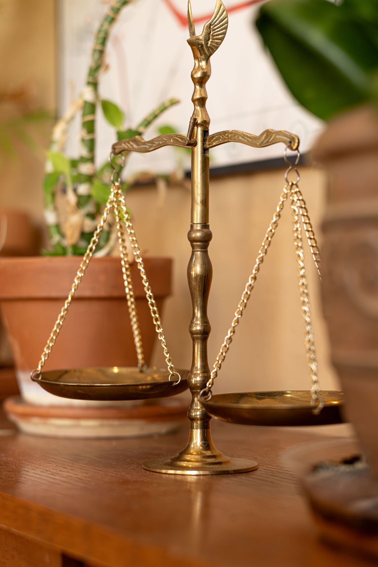 Decorative brass scales of justice with ornate eagle top stand on wooden table near plants.