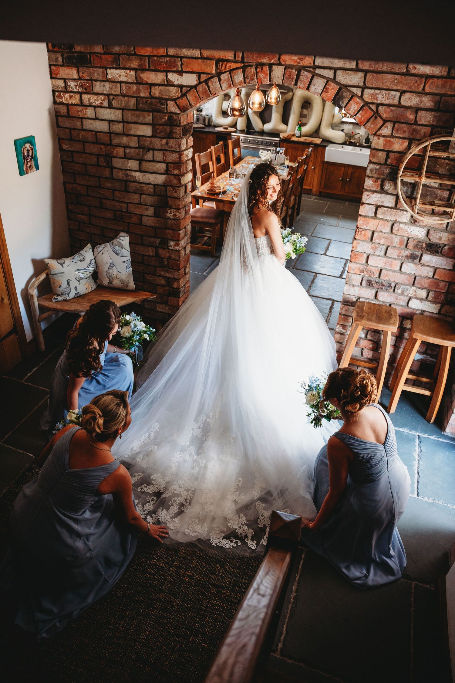 Bride in flowing white tulle gown twirling in sunlit green field with trees and farmhouse backdrop at Tanygraig Farm Aberystwyth