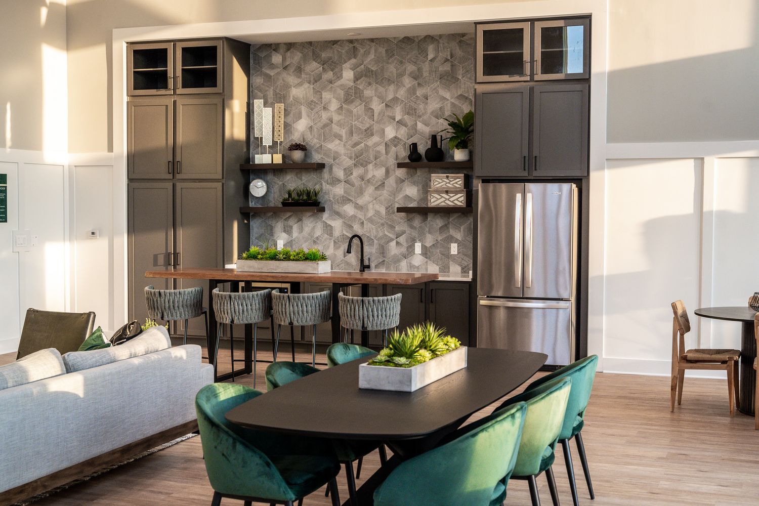 Modern open kitchen and dining area with dark cabinets, emerald green chairs and a textured accent wall.