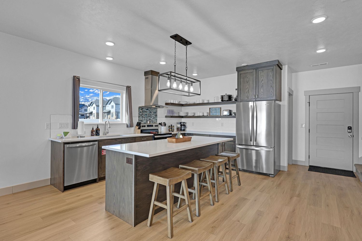 Modern kitchen with gray cabinets, island with bar stools, stainless steel appliances, and light wood floors.