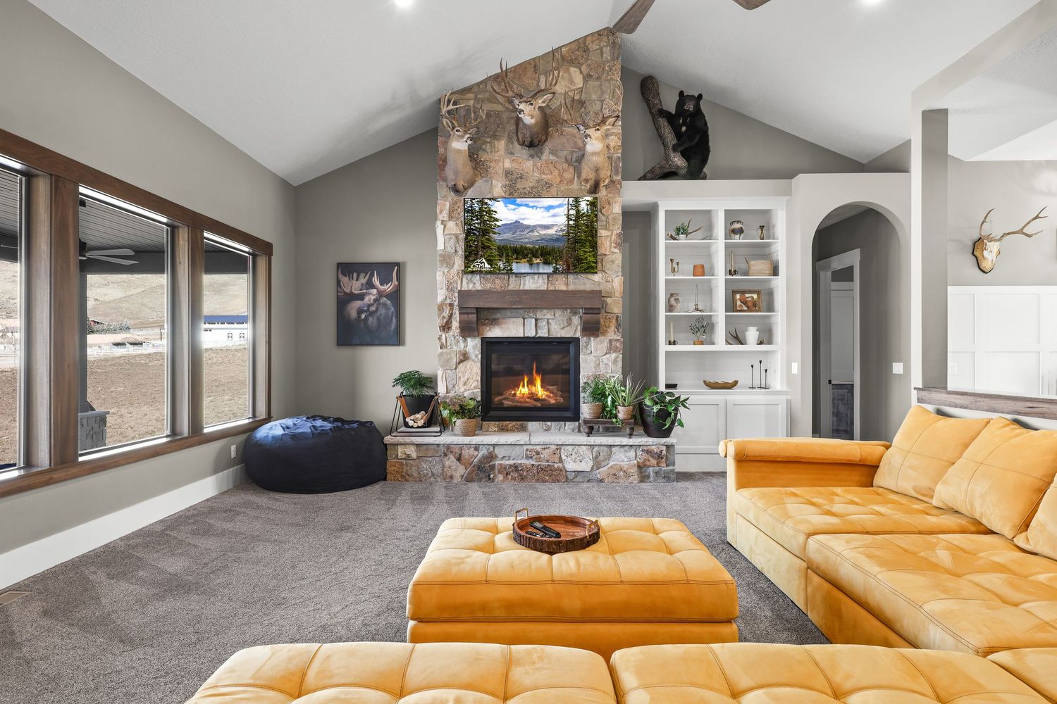 Cozy living room with vaulted ceiling, stone fireplace, built-ins, and gold velvet sectional sofa. Captured by Slate Media (best in UT)