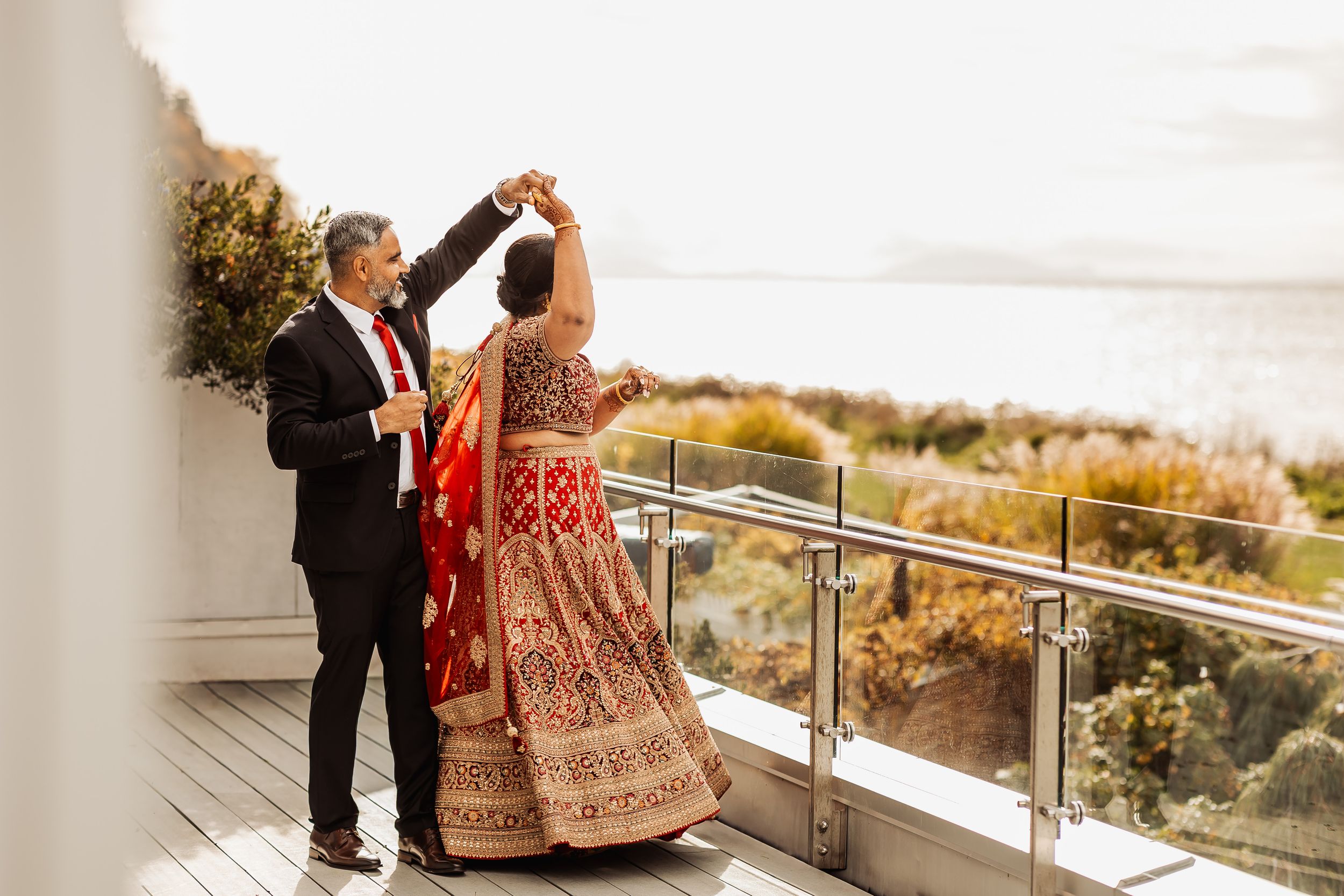 A couple shares a romantic moment on a balcony overlooking a scenic coastal landscape at sunset.