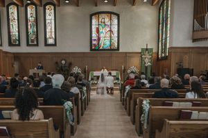 Traditional church wedding ceremony with guests seated in wooden pews beneath colorful stained glass windows.