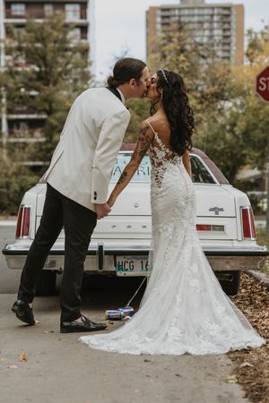 Bride and groom sharing a kiss beside a classic white vintage car after their wedding ceremony.