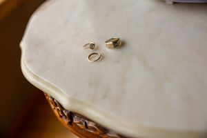 Two gold wedding bands and an engagement ring displayed on a white marble surface before the ceremony.