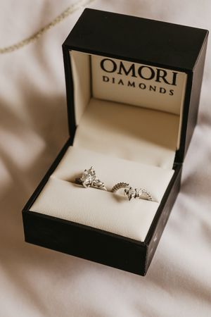 Two diamond rings displayed in Omori Diamonds black jewelry box on white fabric.