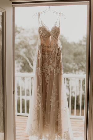 Stunning lace and tulle wedding gown hanging in a sunlit doorway with balcony views in the background.