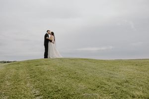Bride and groom share a kiss on a green grassy hill under an overcast sky.