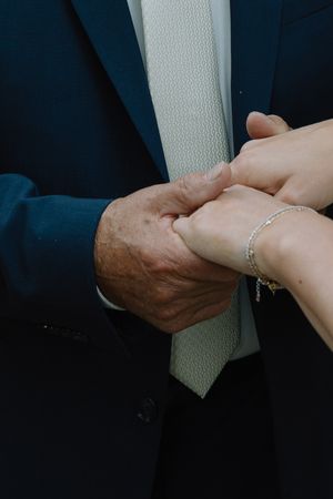 Close-up of elderly hands in navy suit gently holding younger hands wearing a delicate diamond bracelet.