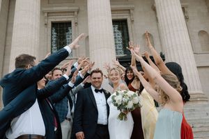 Wedding party celebrating on steps of grand building with hands raised in joy.