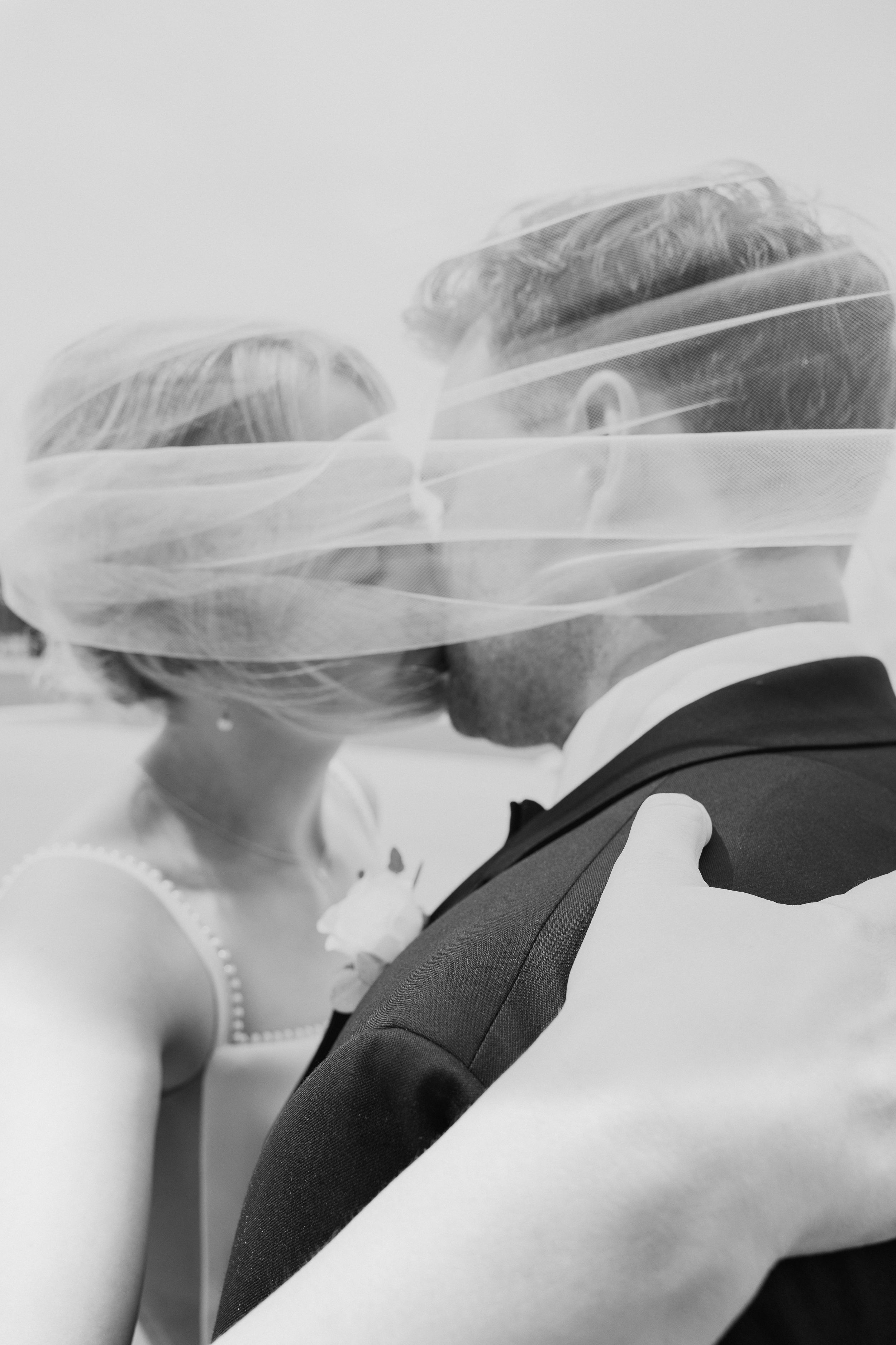 Romantic black and white photo of bride and groom kissing under flowing bridal veil.