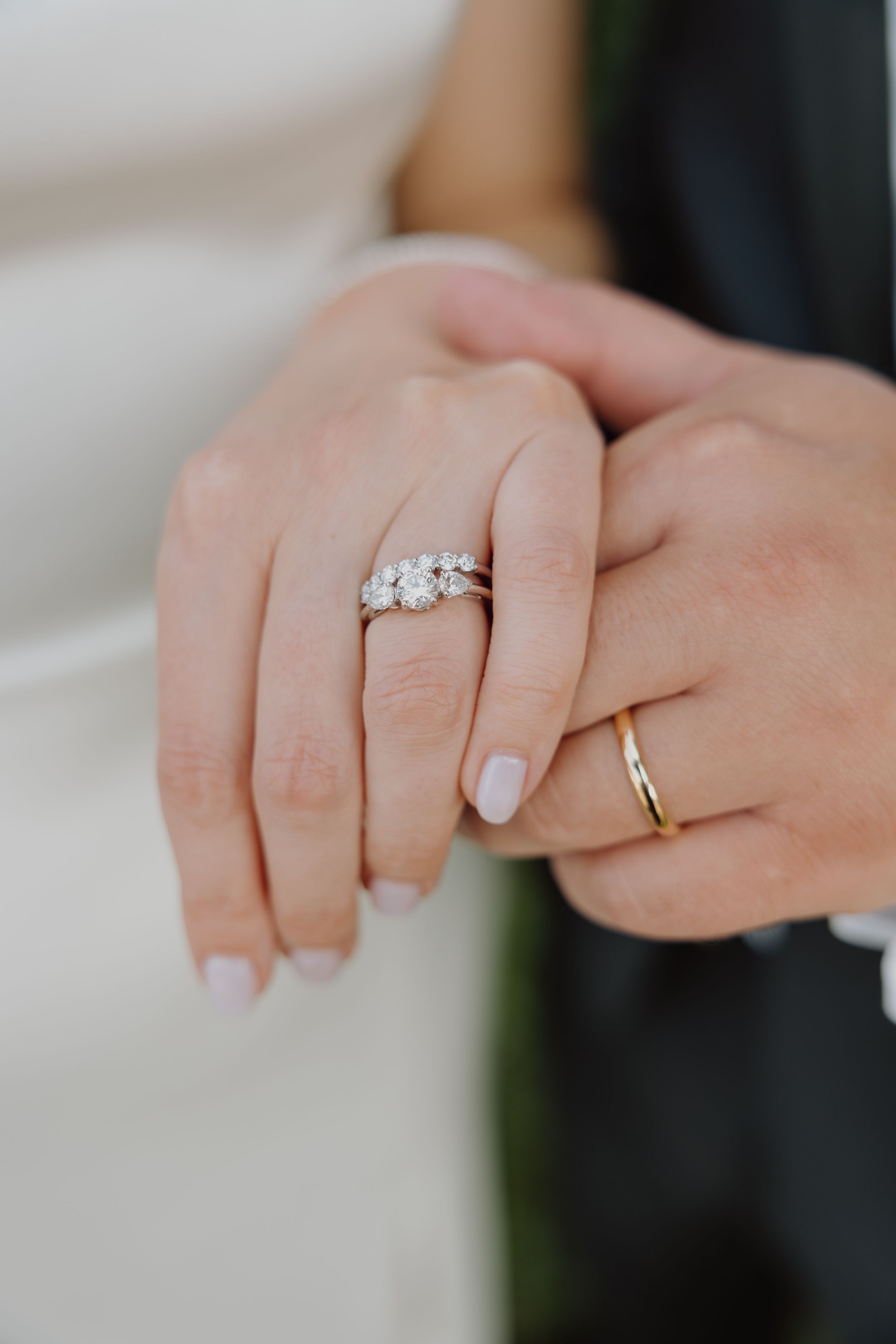 Close-up of bride's three-stone diamond engagement ring and groom's gold wedding band on their hands.