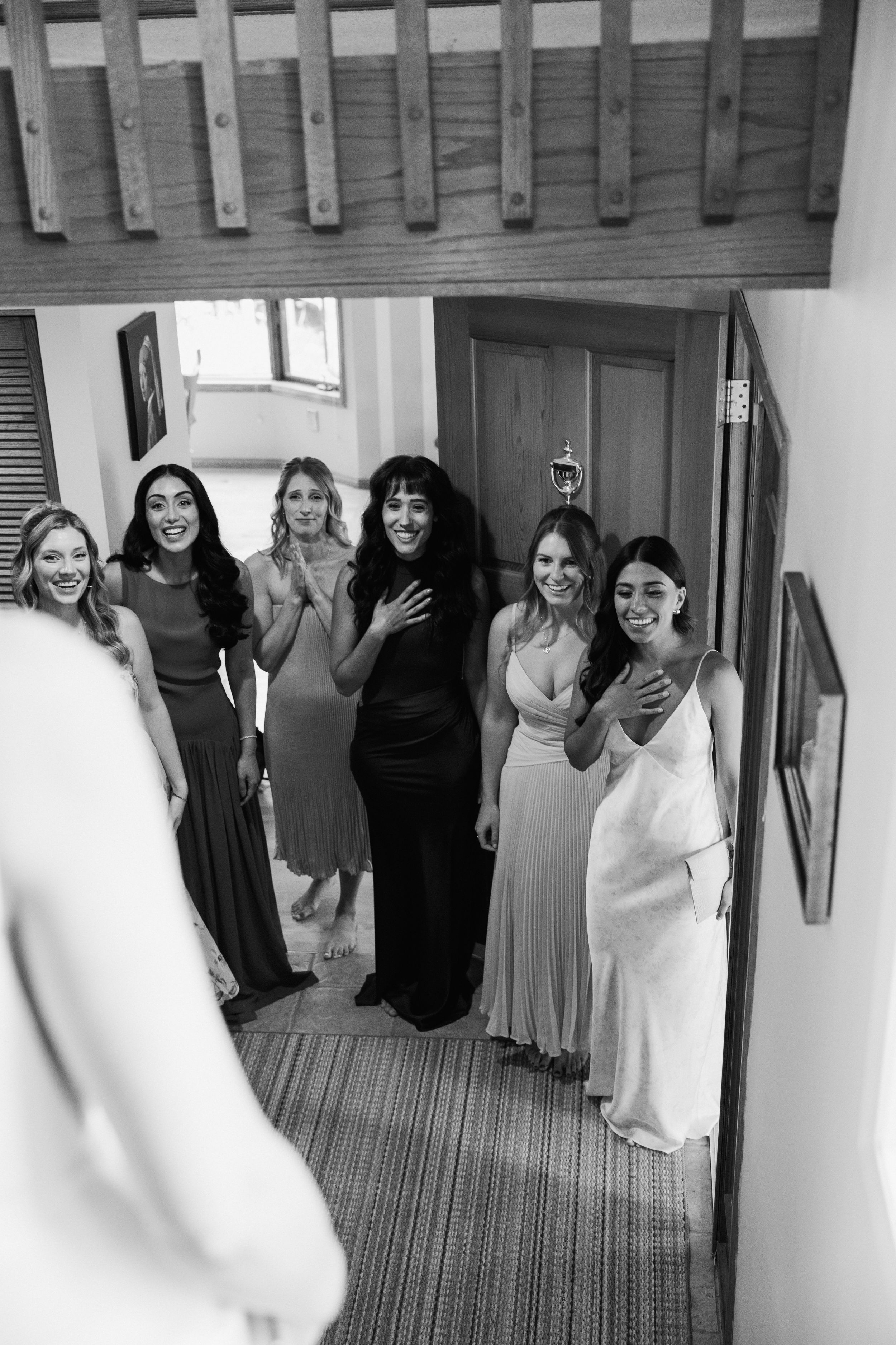 Black and white photo of bridesmaids reacting with joy as bride reveals her wedding dress.