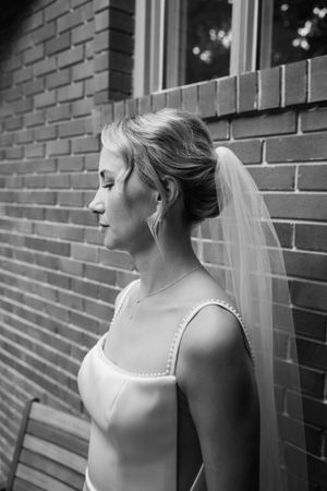 Black and white profile portrait of bride wearing veil and wedding dress against brick wall.
