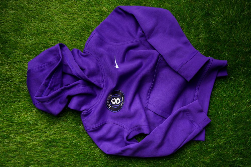 Purple Nike hoodie with False 8 FC logo laid flat on green grass.