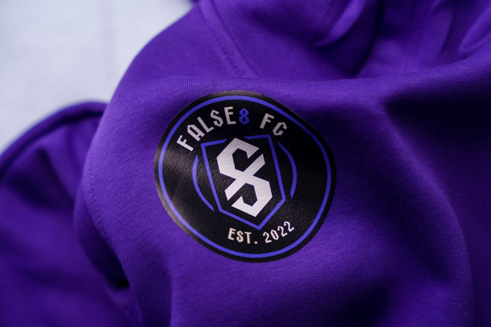 Close-up of False 8 FC soccer team crest on purple fabric showing established 2020 date.