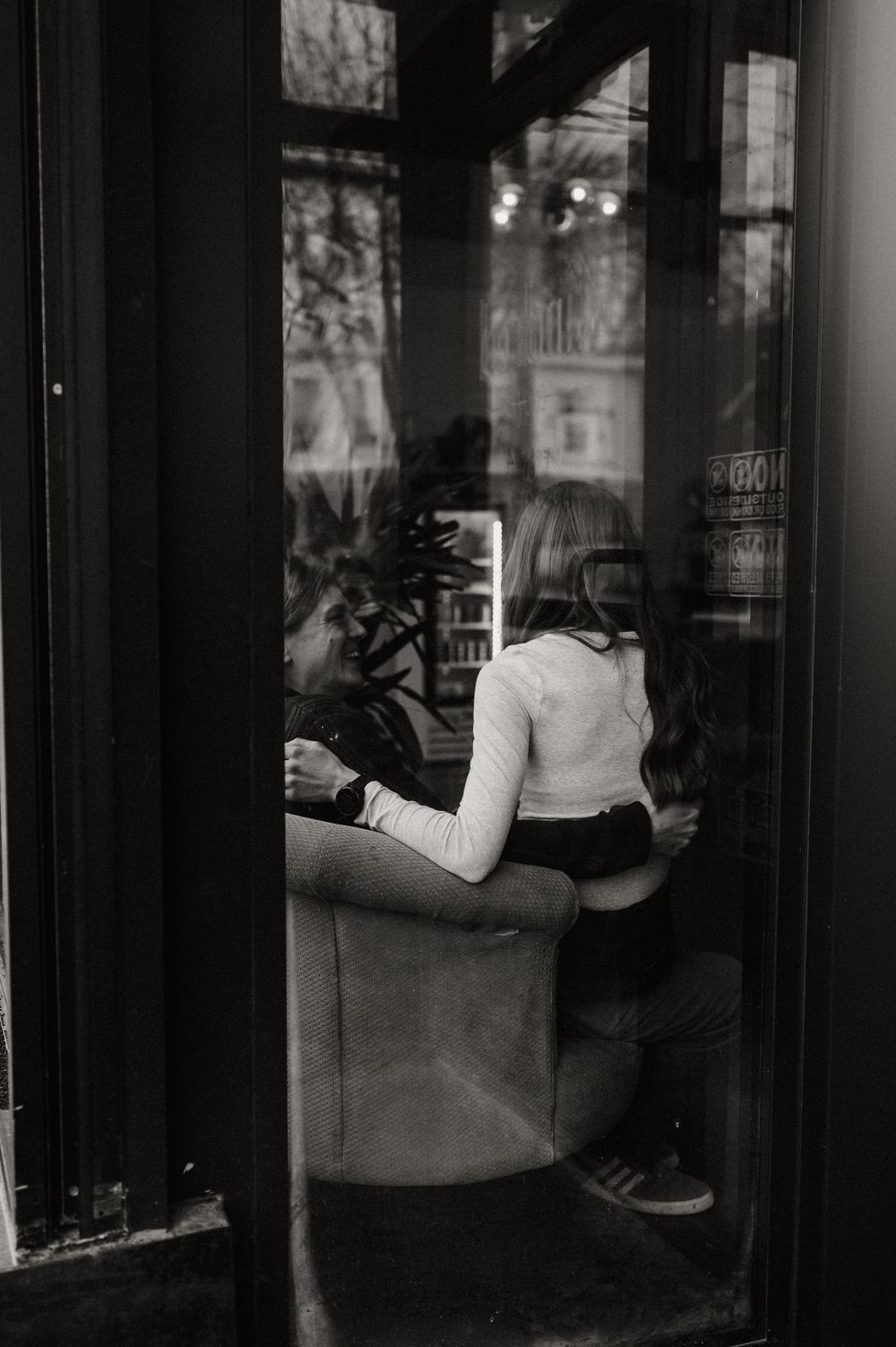 Black and white photograph of a person's reflection in a window display, creating a moody urban composition.