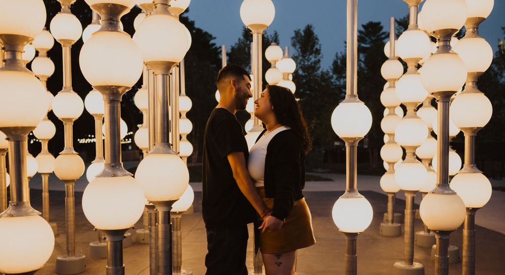 A couple stands close together among decorative white globe lights at dusk.