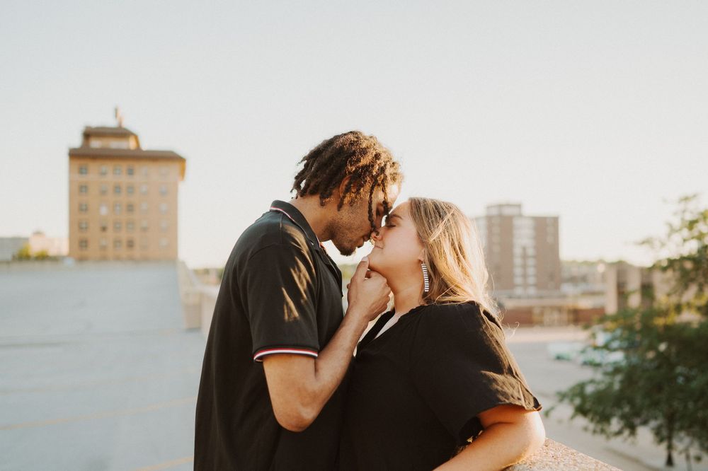 Romantic couple embraces during golden hour sunset with city skyline in background.