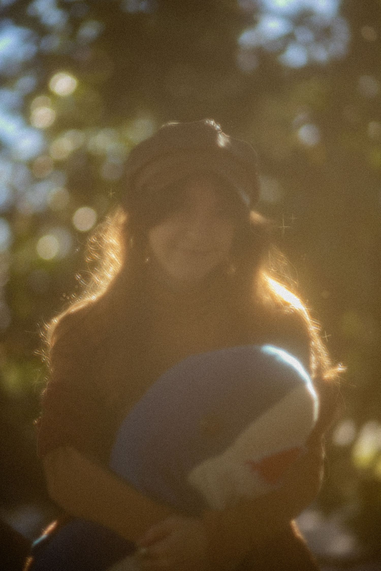 Young woman in hat holding books with golden bokeh sunlight in dreamy outdoor portrait.