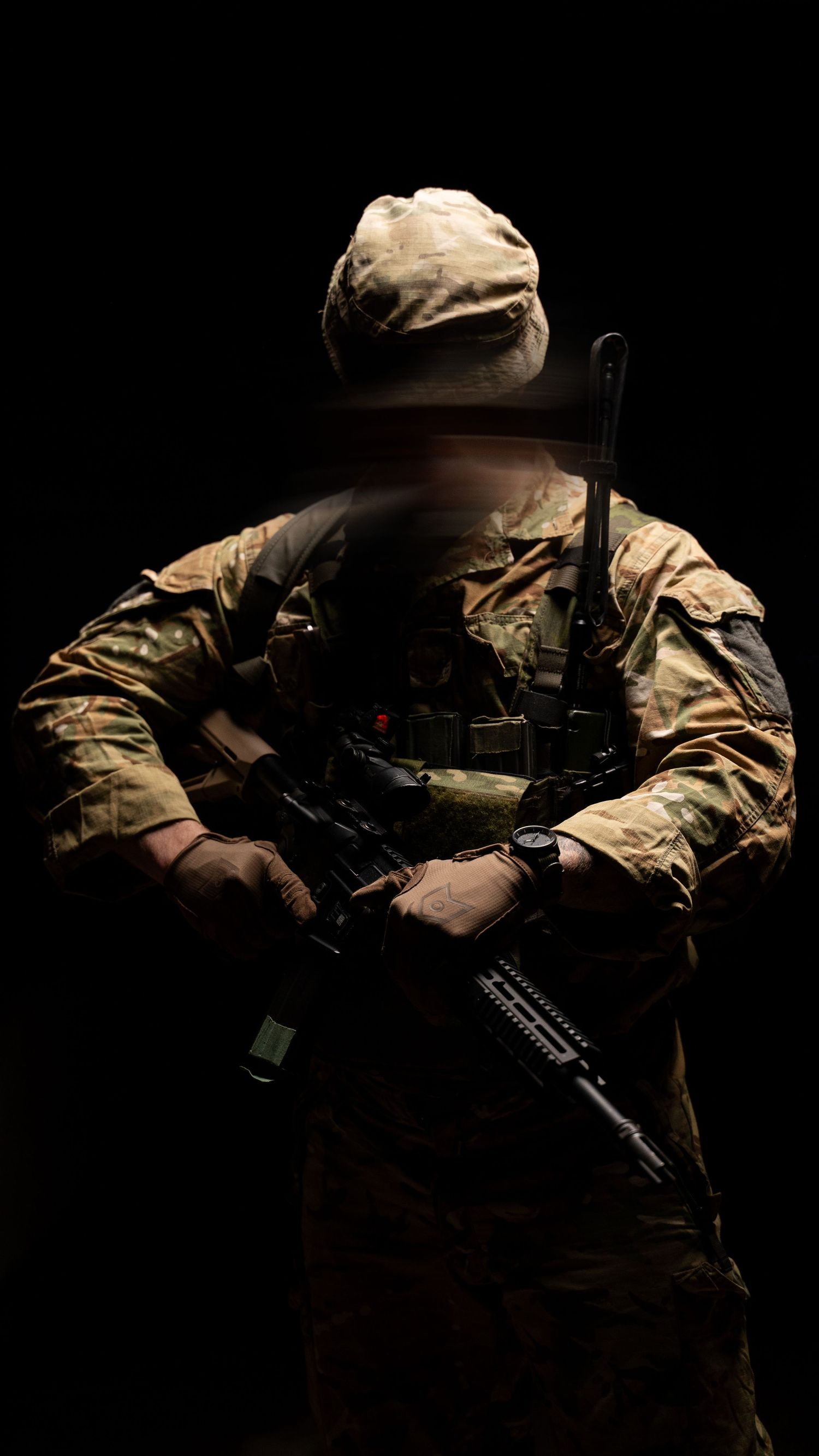 Tactical soldier in camouflage gear holding machine gun with ammunition belt in dramatic red lighting.