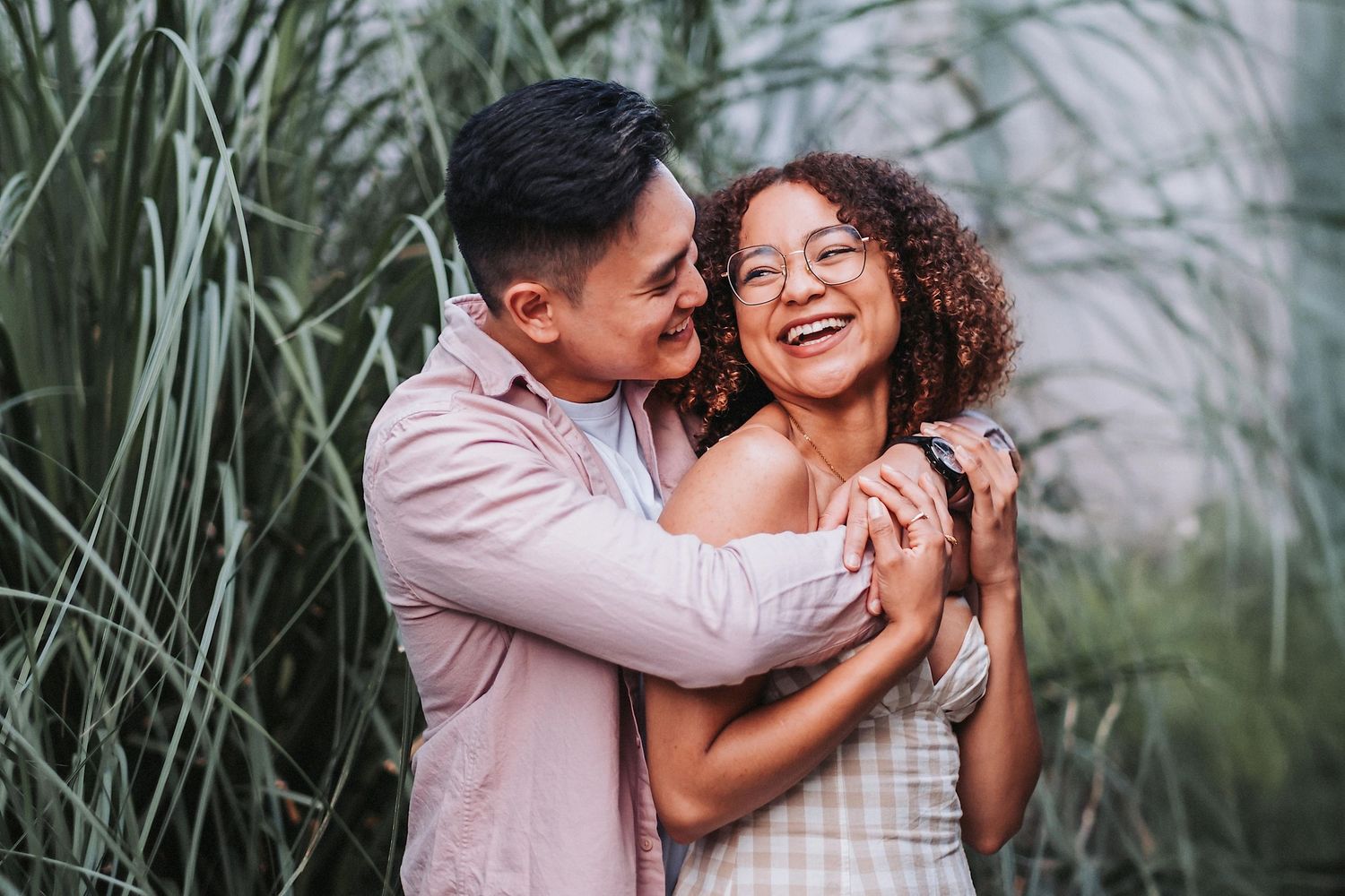 A joyful romantic moment shared between a couple embracing outdoors among tall grasses during a portrait session.