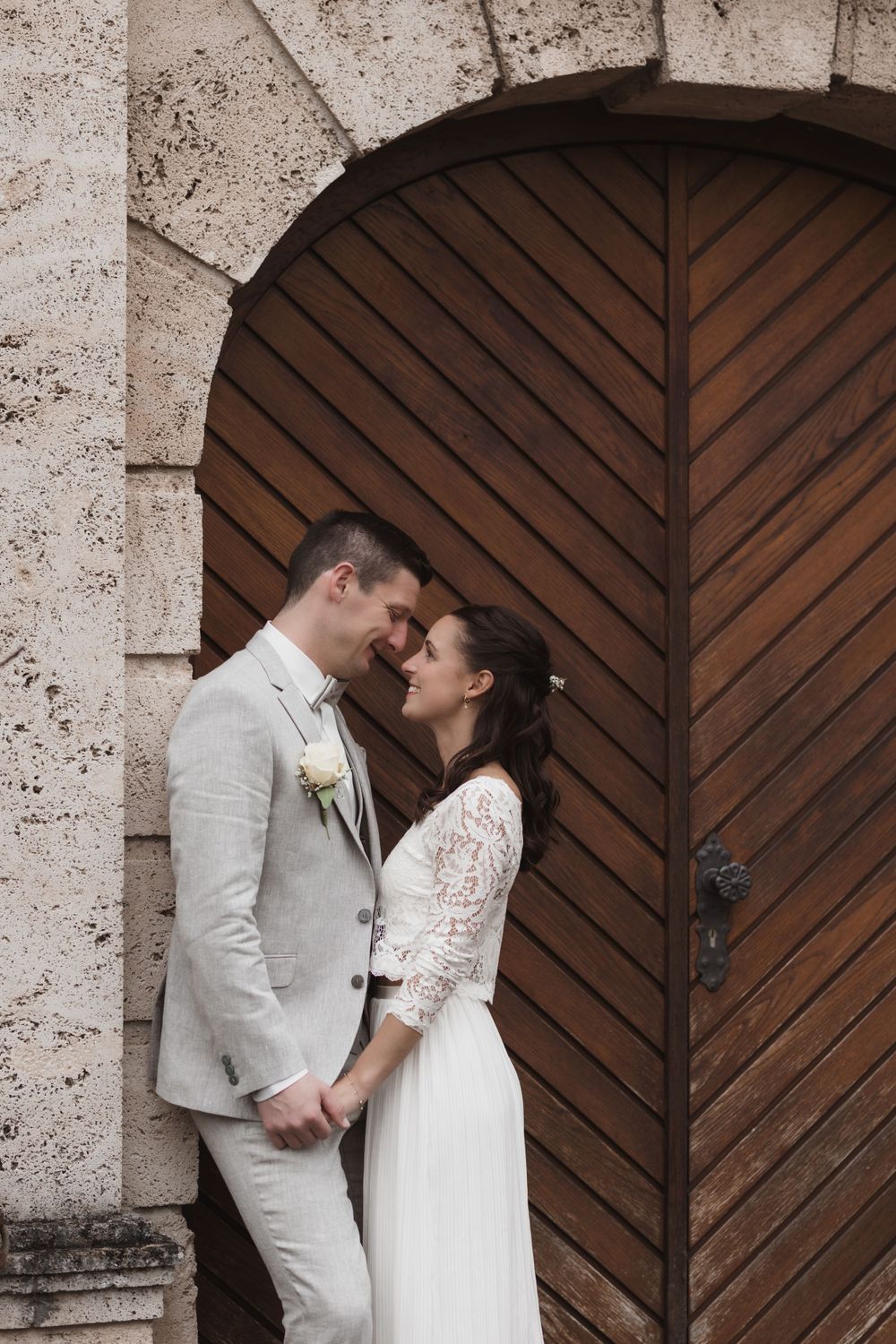 Ein romantisches Hochzeitspaar, das einen intimen Moment vor einer großen Holzbogentür teilt.