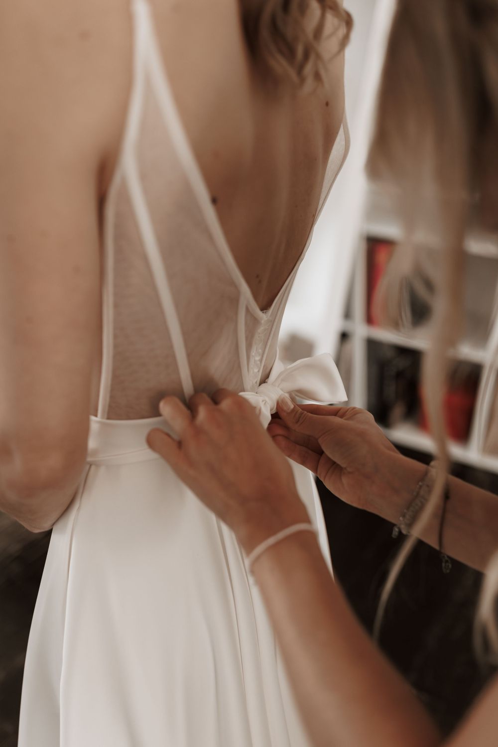 Die Schleife an der Rückseite des eleganten weißen Brautkleides wird vorsichtig von der Trauzeugin gebunden.