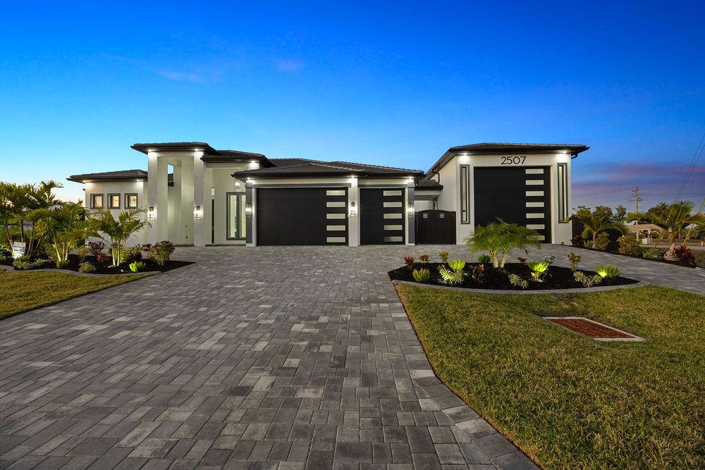 Modern Florida luxury home with paver driveway, three-car garage, and contemporary architecture illuminated at dusk.