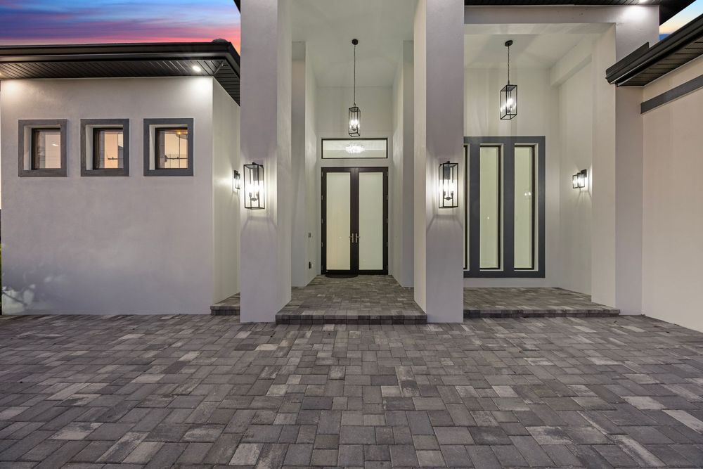 Modern home entrance with gray brick paver courtyard, white stucco walls, pendant lights, and elegant double doors.