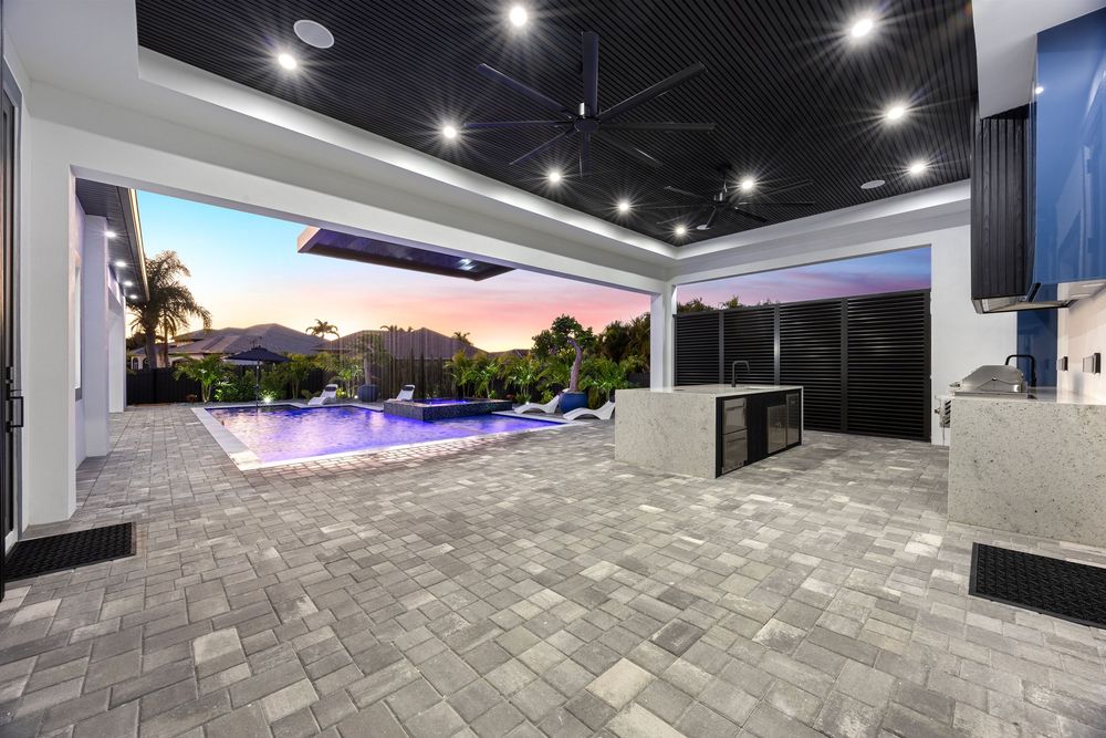 Luxury outdoor patio with pool, twilight sky, recessed lighting, dark ceiling, outdoor kitchen, and elegant stone tile flooring.