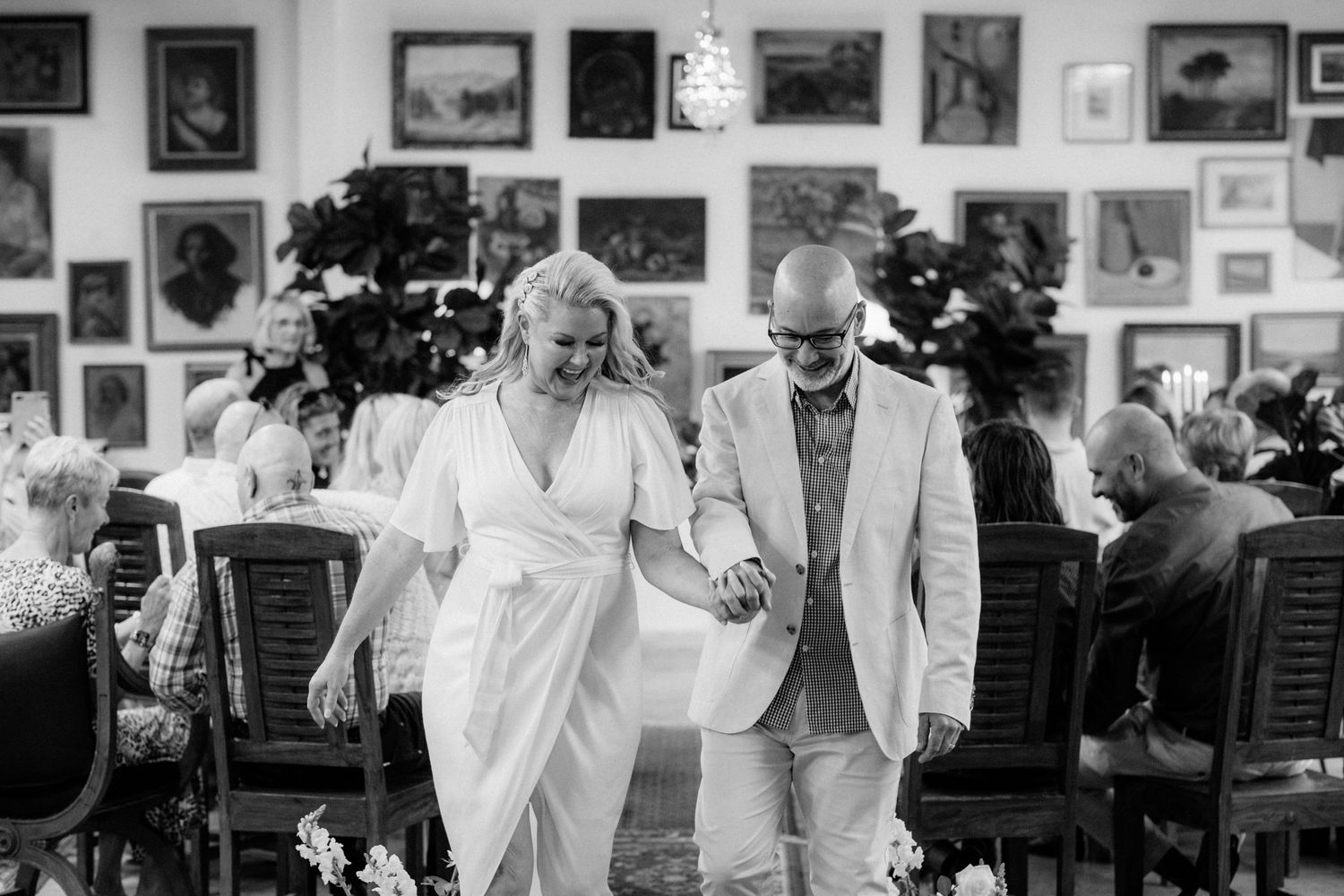 A couple walks together through an art gallery filled with framed paintings.