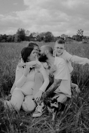 Eine Familie sitzt glücklich auf einer Sommerwiese. Die Geschwister lachen. Alle haben Spaß und kuscheln sich zusammen.
