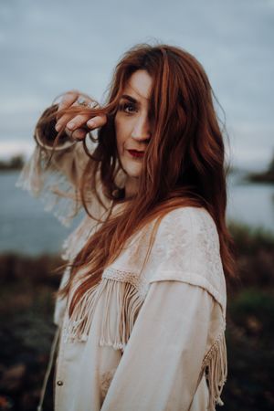 Ein Frau steht während eines Portraitshooting mit Hey Elli Fotoreportagen vor der Elbe und hält ihre Hand an ihr Gesicht. Ihr Haar ist rot.