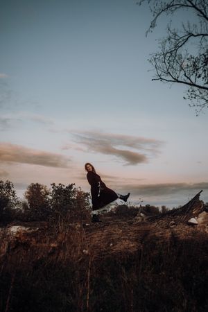 Ein Frau steht während eines Portraitshooting mit Hey Elli Fotoreportagen auf einem Baumstumpf in einem Mantel. Sie streckt ihr Bein.