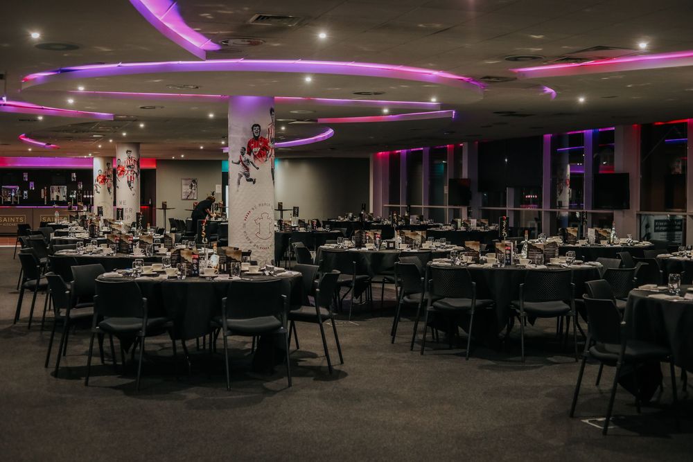 Modern reception hall with purple LED lighting and round tables set for dining.