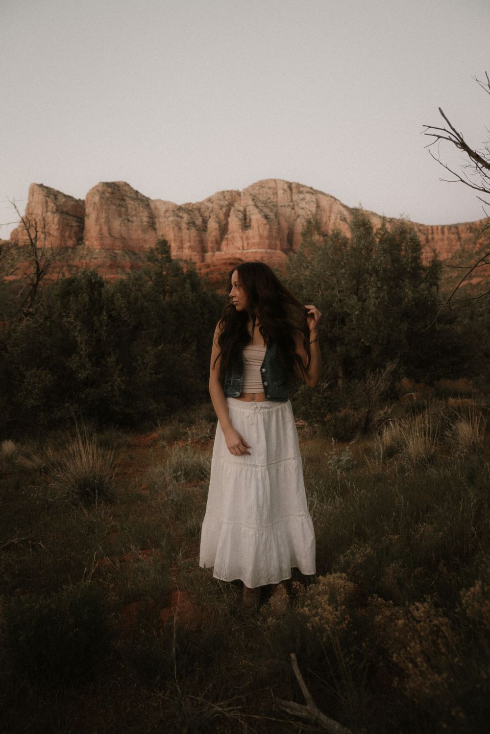Woman in white dress standing against backdrop of red rock formations at sunset.