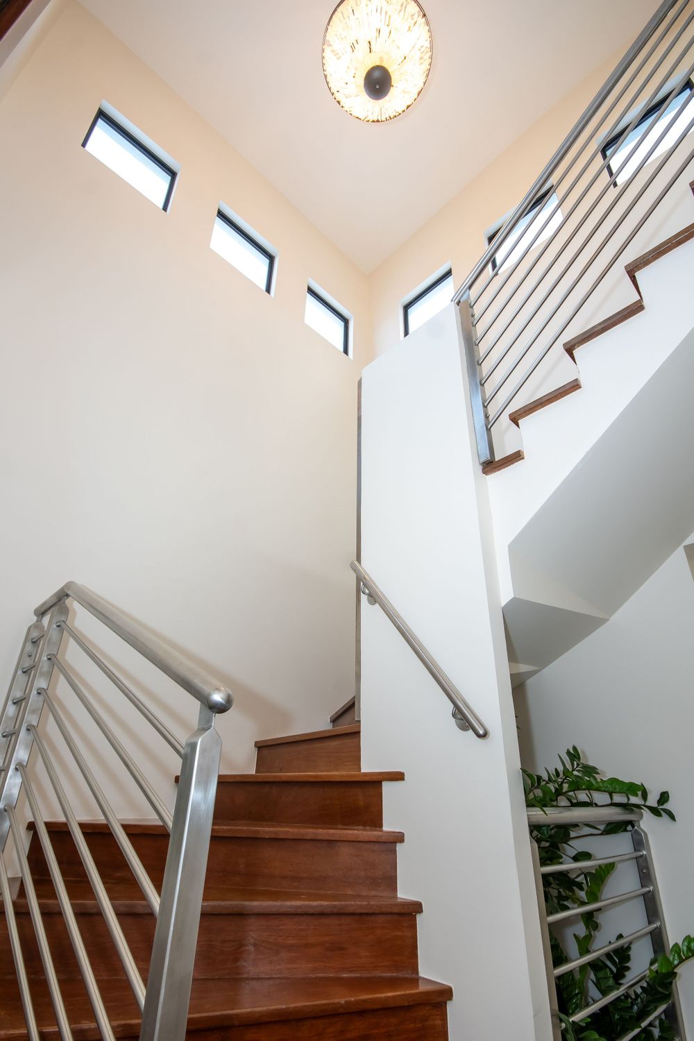 Modern staircase with wooden steps, metal railings, and high ceiling featuring clerestory windows.