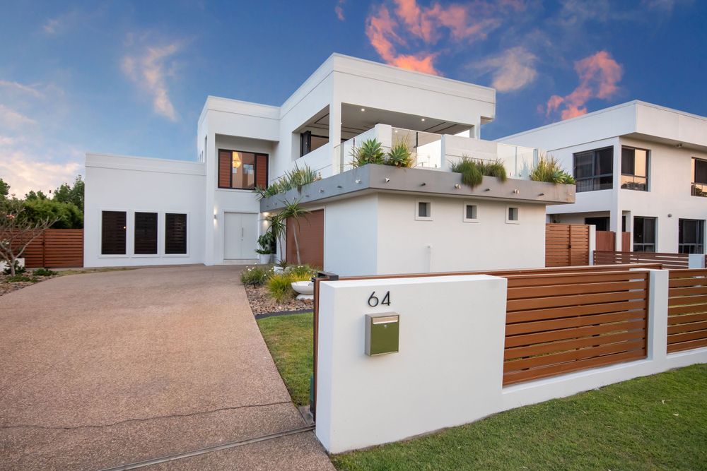 Modern white architectural home with wooden fence and rooftop garden at dusk.