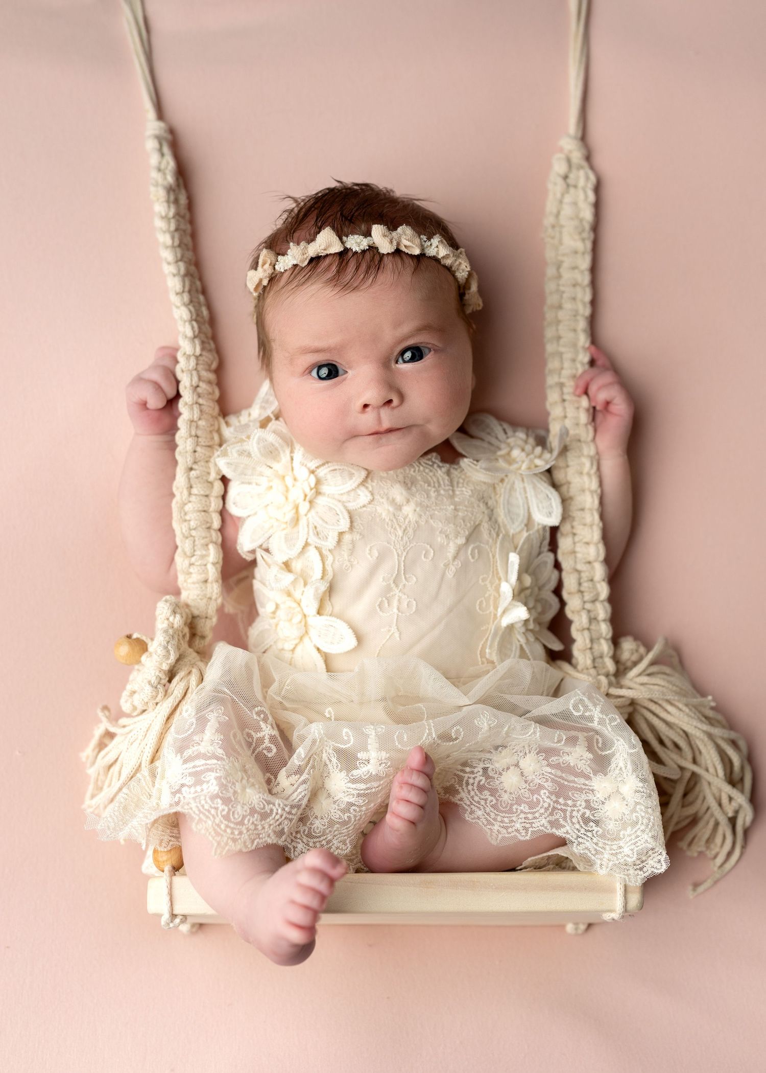 Two peaceful sleeping newborn twins nestled together in a cream-colored hammock.