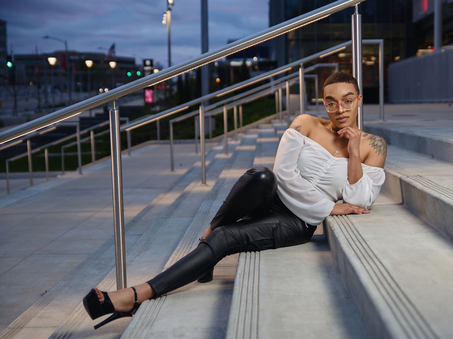 Model in white top and black pants poses on concrete steps at dusk.
