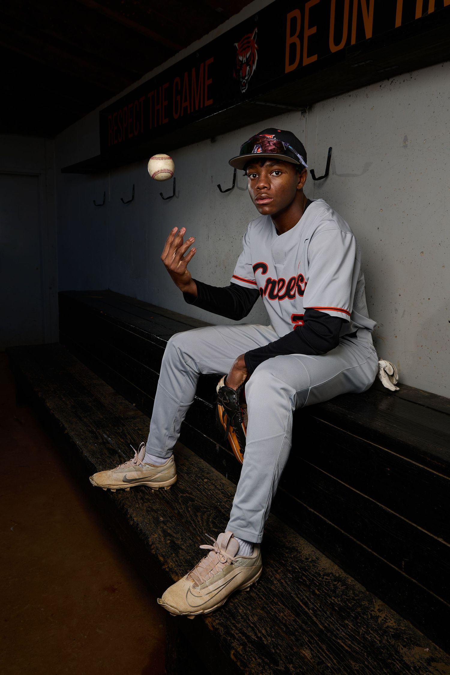 Baseball player in white uniform sitting in dugout wearing cream colored sneakers.