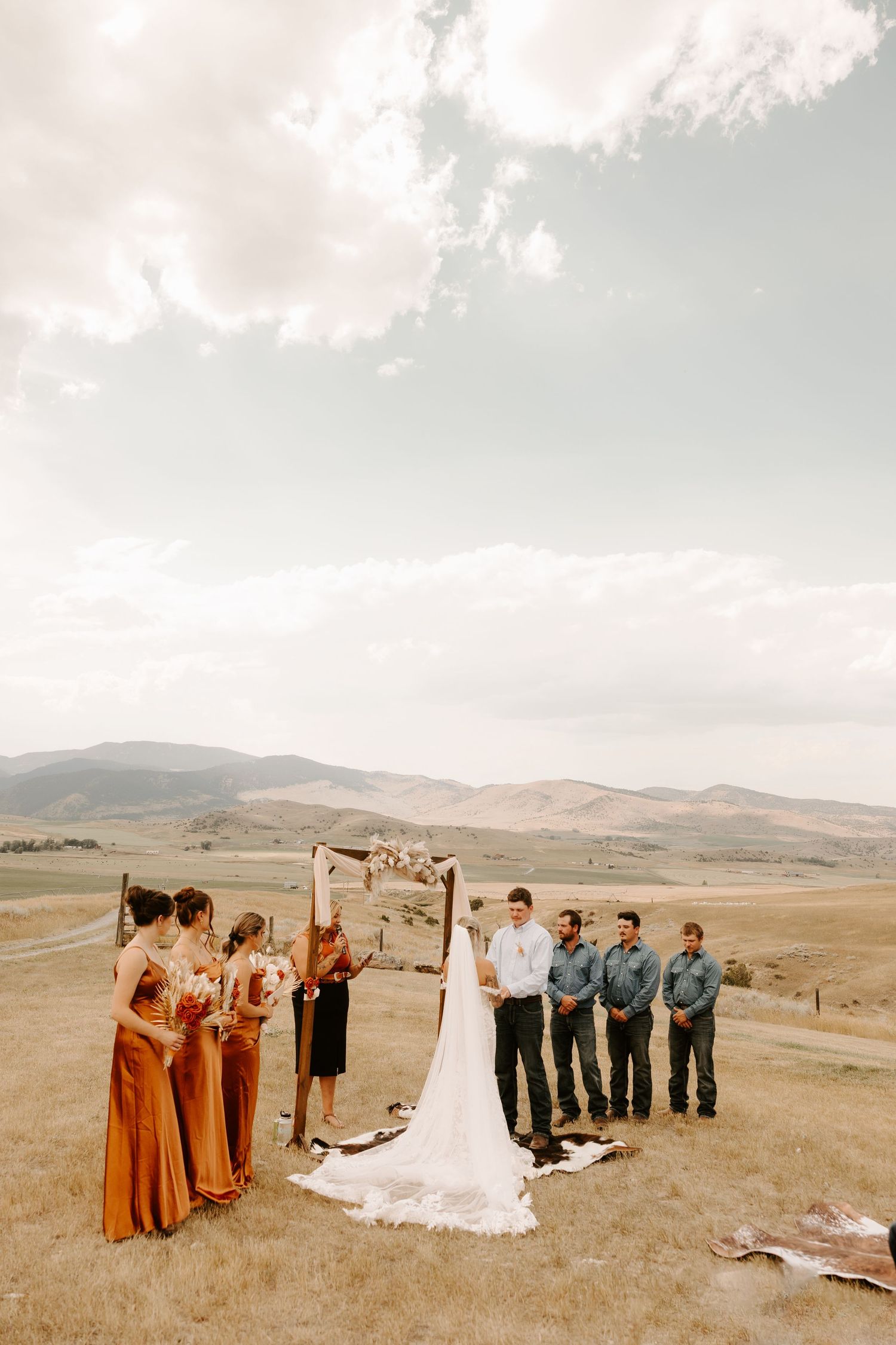 Outdoor wedding ceremony in a scenic mountain landscape with bridal party in rust-colored dresses in Colorado.