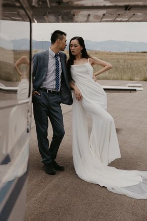A stylish couple poses against a small aircraft during an aviation-themed wedding shoot.