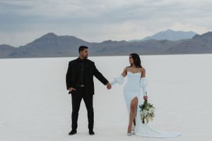 Two people stand together on salt flats with mountains in background during a wedding shoot.