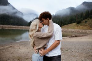 A couple shares an intimate moment by a mountain lake shrouded in morning mist.