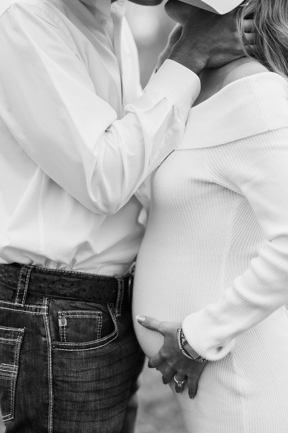A black and white closeup of two people in white tops holding hands intimately, one wearing jeans and one in a sweater.