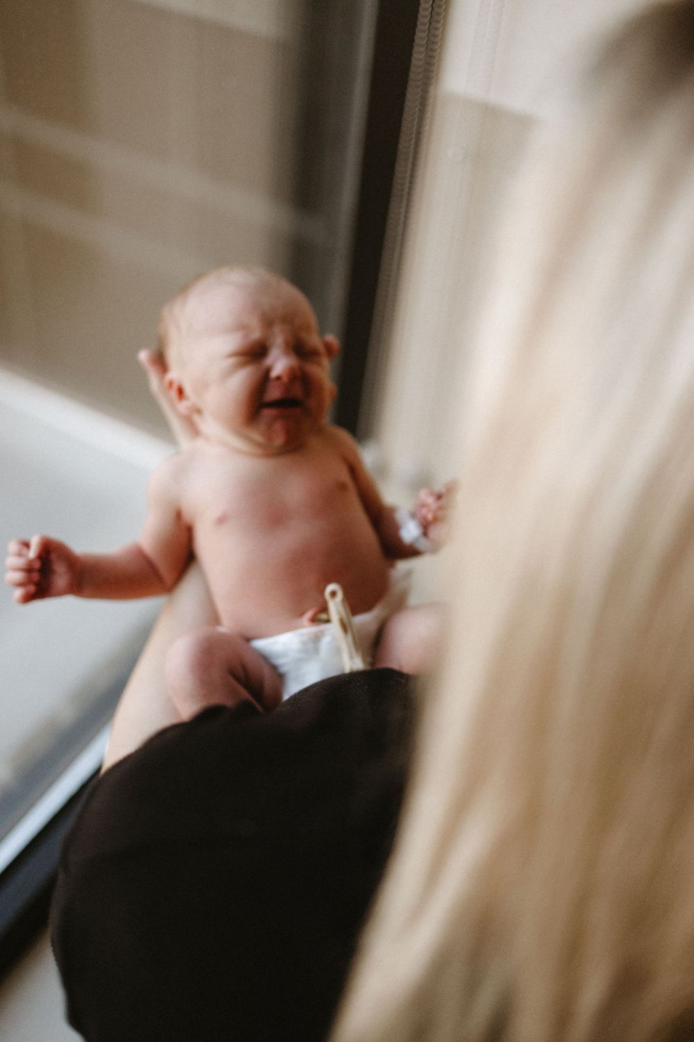 A laughing baby lies on their back in soft window light creating a candid moment.