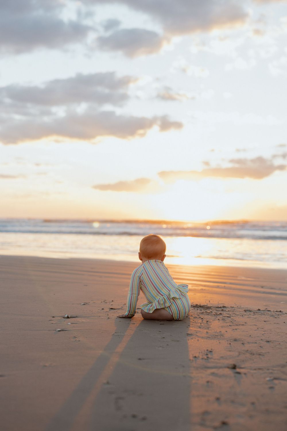 A solitary figure sits on the beach watching a golden sunset over the ocean.